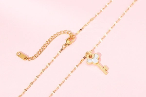 Detail of gold water wave chain with shell-inlaid key pendant and lobster clasp