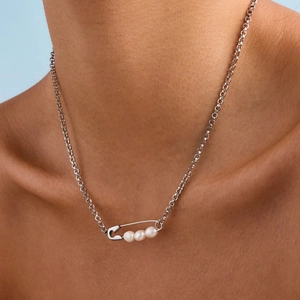 Close-up of a silver safety pin pendant necklace with white pearls worn by a model