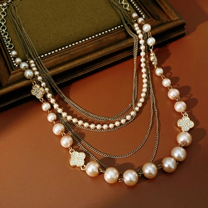 Detail of multi-layer pearl necklace with gold chains and diamond-set clover pendant