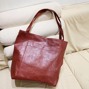 Vue détaillée du grand sac cabas en cuir marron rouge posé sur un canapé beige