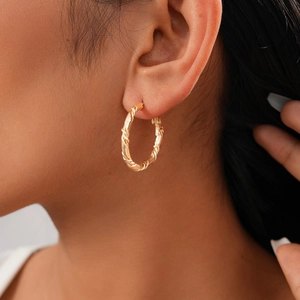 Close-up of golden twisted texture hoop earrings worn by a model for a chic look