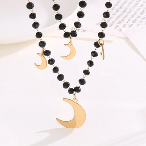 Macro shot of gold moon pendant with black beaded chain on a white surface