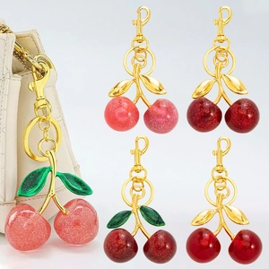 Chic resin cherry keychains in multiple colors with gold hardware on a beige handbag