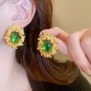 Macro detail of vintage gold earrings with green gemstones and textured leaf design
