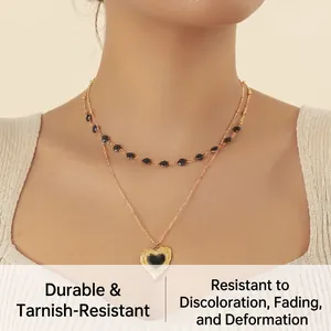Detailansicht einer goldenen Doppelkette mit schwarzen Perlen und einem Herzanhänger