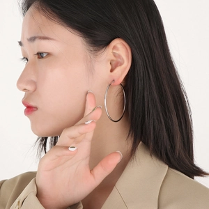 Close-up of a model wearing large silver-tone stainless steel hoop earrings in a minimalist style