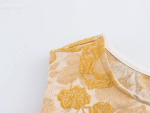 Nahaufnahme von goldenem Jacquard-Stoff mit floralen Mustern am ärmellosen Oberteil