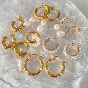 Collezione di orecchini a cerchio dorati con perle barocche e strass su piatto di vetro