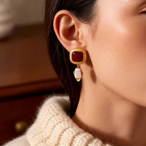 Vintage gold textured earrings with dark red gem and white drop pendant on a model