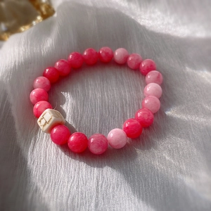 Close-up of pink ceramic beaded bracelet with white textured square bead on soft white fabric