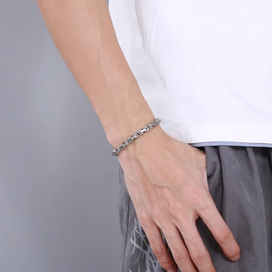 Close-up of a silver stainless steel square link chain bracelet worn by a male model