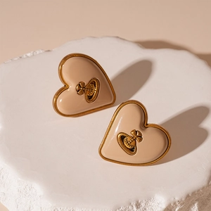 Détail de boucles d'oreilles cœur beige avec logo orbe Saturne doré sur pierre texturée