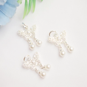 Detailed view of silver bow pendants with white pearls on a soft white fabric background