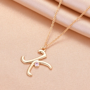 Macro shot of gold letter K pendant with pink gemstone on soft peach silk background