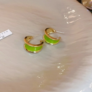 Detail of C-shaped gold-plated earrings with vibrant green enamel inlay on beige surface
