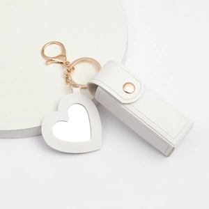 Close-up of white PU leather lipstick holder with gold hardware and heart mirror charm