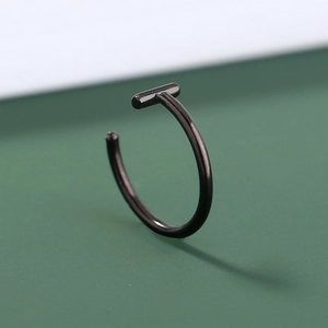 Close-up of a sleek black stainless steel U-shaped nose ring on a green background