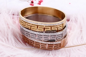 Detailed view of hollow meander pattern bangles with pavé diamonds in three gold tones