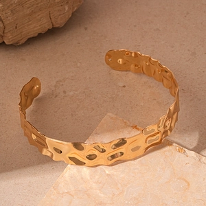Detail of gold hammered texture open cuff bracelet with irregular metallic surface