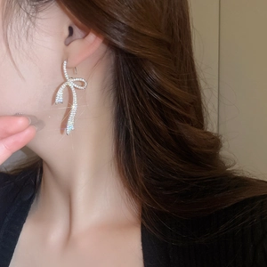 Close-up of sparkling bow tassel earrings with zircon crystals on a model's ear