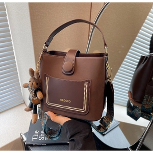 Brown bucket bag detail with WEGOCO logo, wide patterned strap and plush rabbit charm