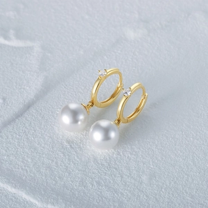 Detailed shot of gold pearl drop earrings with zircon inlay on a gray stone surface