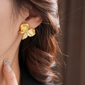 Close-up of golden irregular floral earrings with rhinestones on a female model