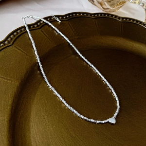 Macro shot of silver heart pendant with textured crushed silver chain in a vintage tray