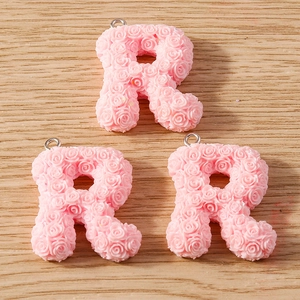 Macro detail of three pink resin letter R charms with relief rose pattern for DIY crafts