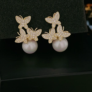 Macro shot of gold butterfly stud earrings with sparkling crystals and large white pearls