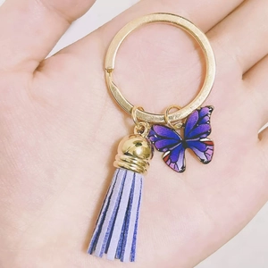 Golden butterfly keychain with purple gradient charm and suede tassel held in hand