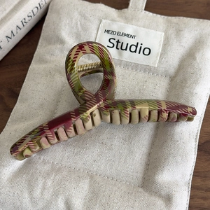 Détail d'une pince à cheveux vintage à carreaux rouges et verts sur un sac en toile