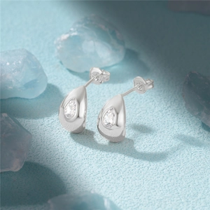 Macro shot of 925 sterling silver teardrop stud earring with clear crystal on blue surface