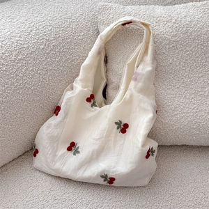 Close-up of red cherry embroidery on white textured fabric of a chic tote bag