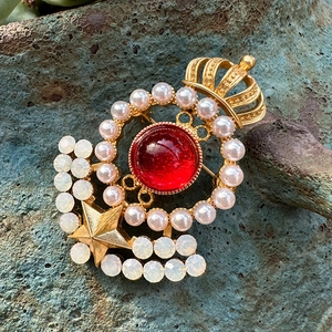 Detail of vintage gold brooch with large red gemstone, pearls, and star on blue stone