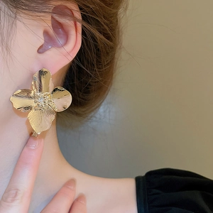 Macro shot of large golden flower stud earrings with detailed metallic texture and center dots