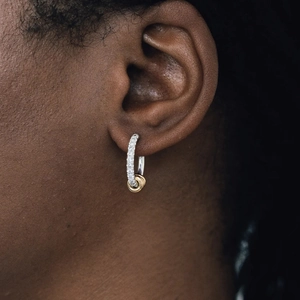 Close-up of model wearing two-tone interlocking hoop earrings with small white crystals