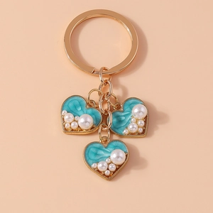 Detail of golden heart keychains with blue enamel inlay and white pearl accents