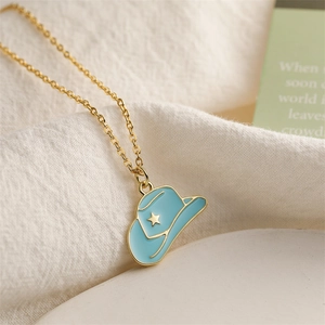 Gros plan d'un collier doré avec pendentif chapeau de cowboy en émail bleu sur tissu blanc