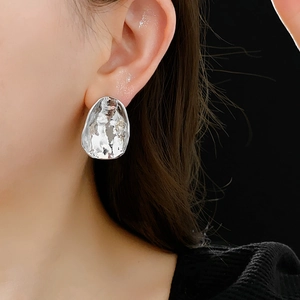 Detail of silver irregular hammered metal earring shown on model with black background