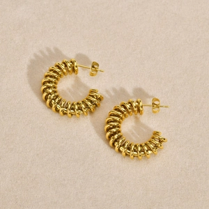 Macro detail of golden C-shaped twisted spiral hoop earrings with polished metal finish