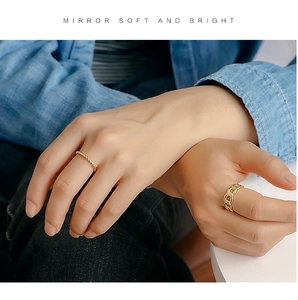 Detail of twisted gold rope ring and link chain design on model hand with denim fabric