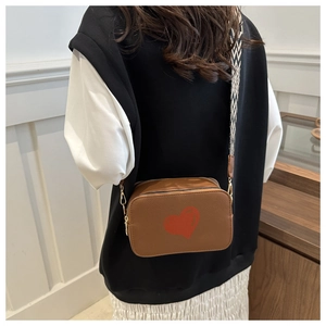 Brown camera bag detail showing red heart pattern and geometric patterned wide strap