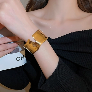 Detail of wide gold wave-edged cuff bracelet with rectangular cutout on model wrist