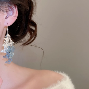 Détail d'une boucle d'oreille papillon ajourée avec pompon bleu clair sur un mannequin