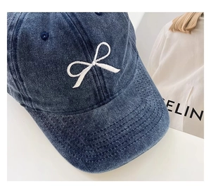 Detailansicht der dunkelblauen Denim-Kappe mit weißer Schleifenstickerei und Nähten
