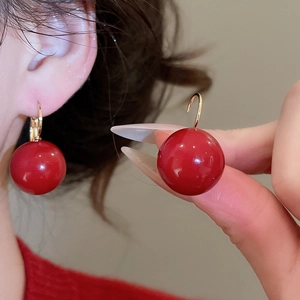 Close-up of red resin spherical earrings with high-gloss finish and gold plating