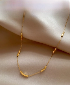 Close-up of gold beaded stainless steel necklace on elegant champagne satin fabric
