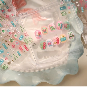 Detail of Mahjong themed nail stickers and press-on nails in pink and gold tones