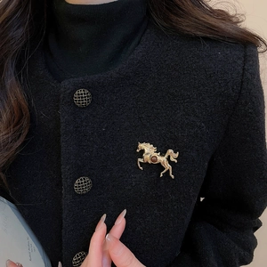 Detail of a golden horse brooch with brown gemstone on a black tweed blazer